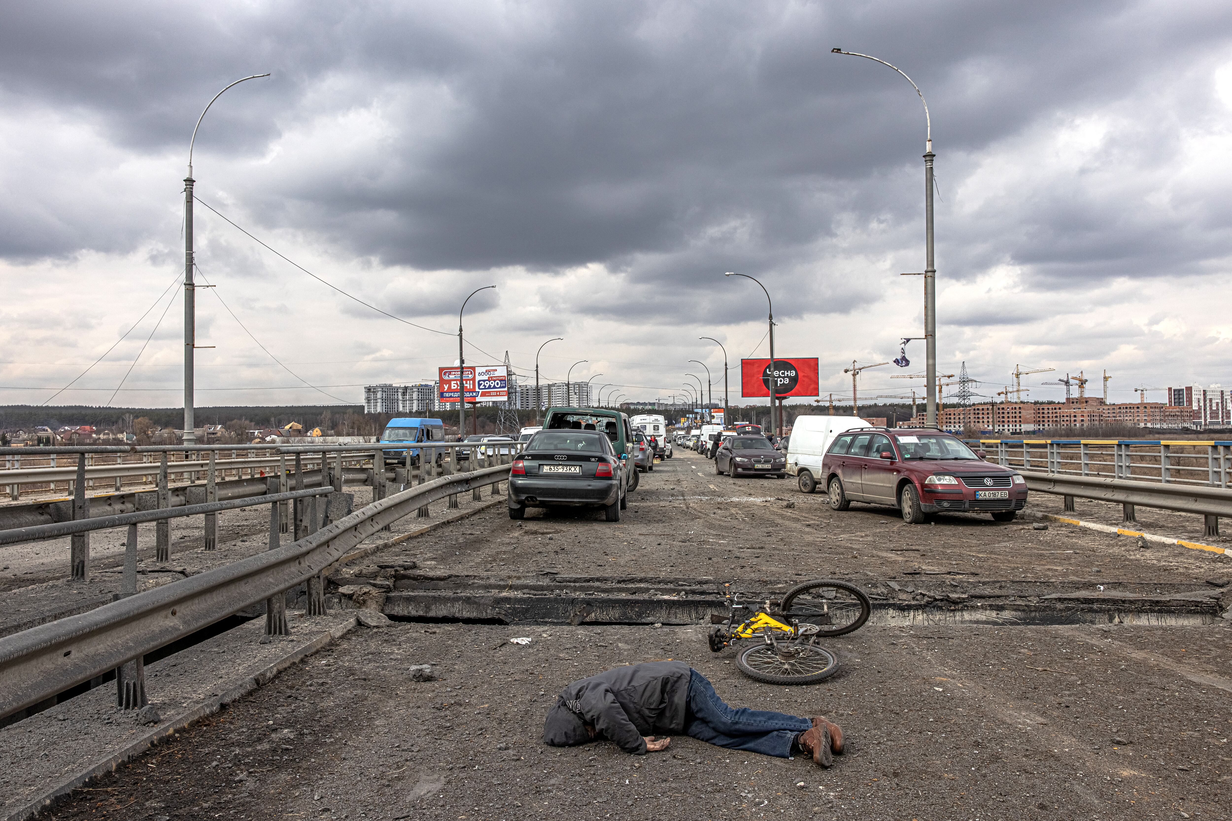 El cuerpo de un hombre muerto yace en un puente destruido junto a los coches abandonados que dejaron las personas que huían de la ciudad de Irpin, en el frente.