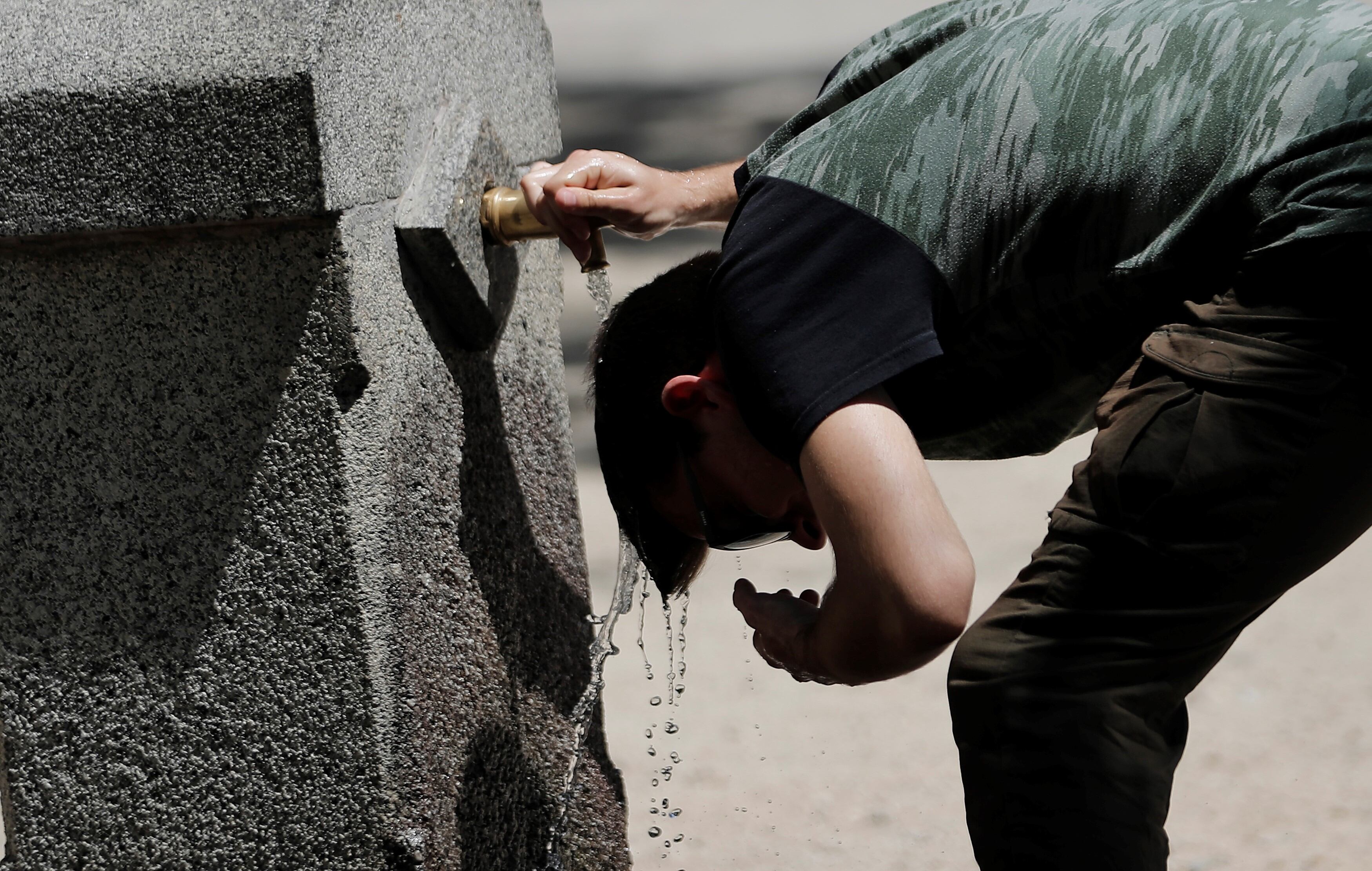 Un hombre se refresca en una fuente de agua.