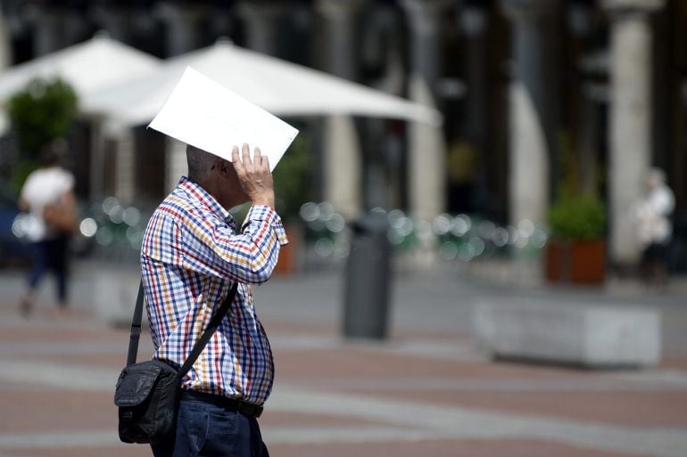 Un hombre se protege la cabeza del sol con unos papeles mientras cruza la plaza Mayor de Valladolid