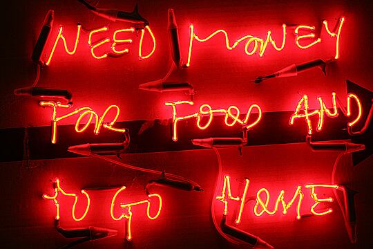 Obra titulada <i>Miserias Ilimitadas</i>. Cartel de cartón con luces de neón que piden "dinero para comer y para ir a casa".  Del artista español Javier Núñez Vasco. (Fotografía de A.O. Goriainoff).