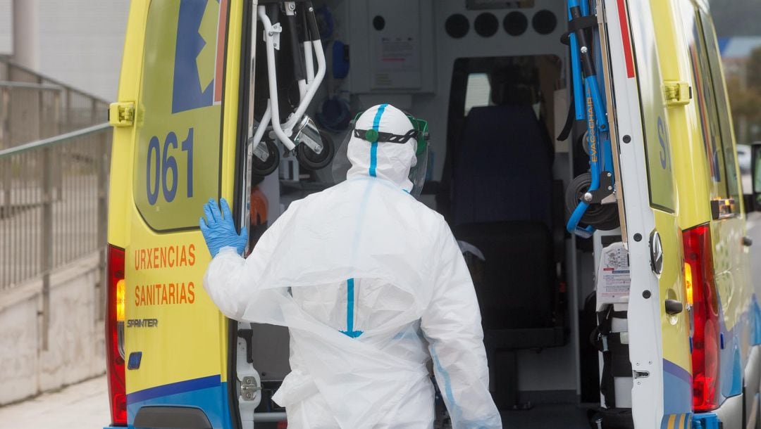 Un trabajador sanitario totalmente protegido cierra la puerta de una ambulancia