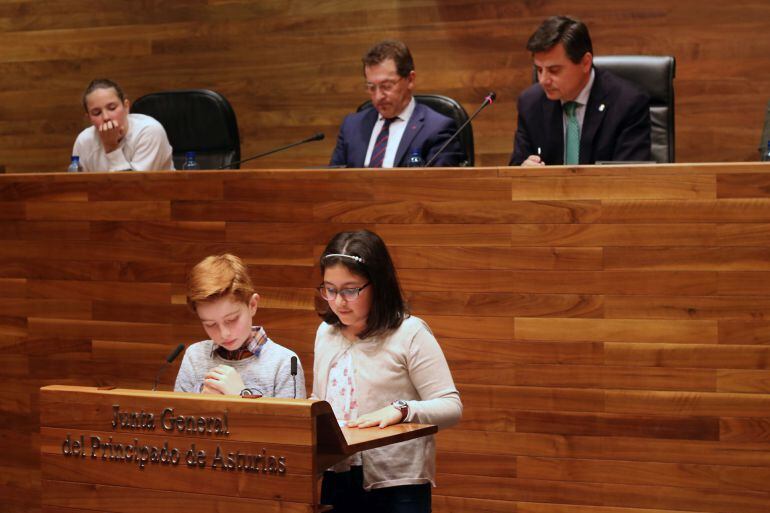 Escolares leen en asturiano en el atril del parlamento asturiano. En la mesa de la cámara escuchan el presidente de la Junta General del Principado, Pedro Sanjurjo y el consejero de Educación, Genaro Alonso. Acto institucional con motivo de la Selmana de 