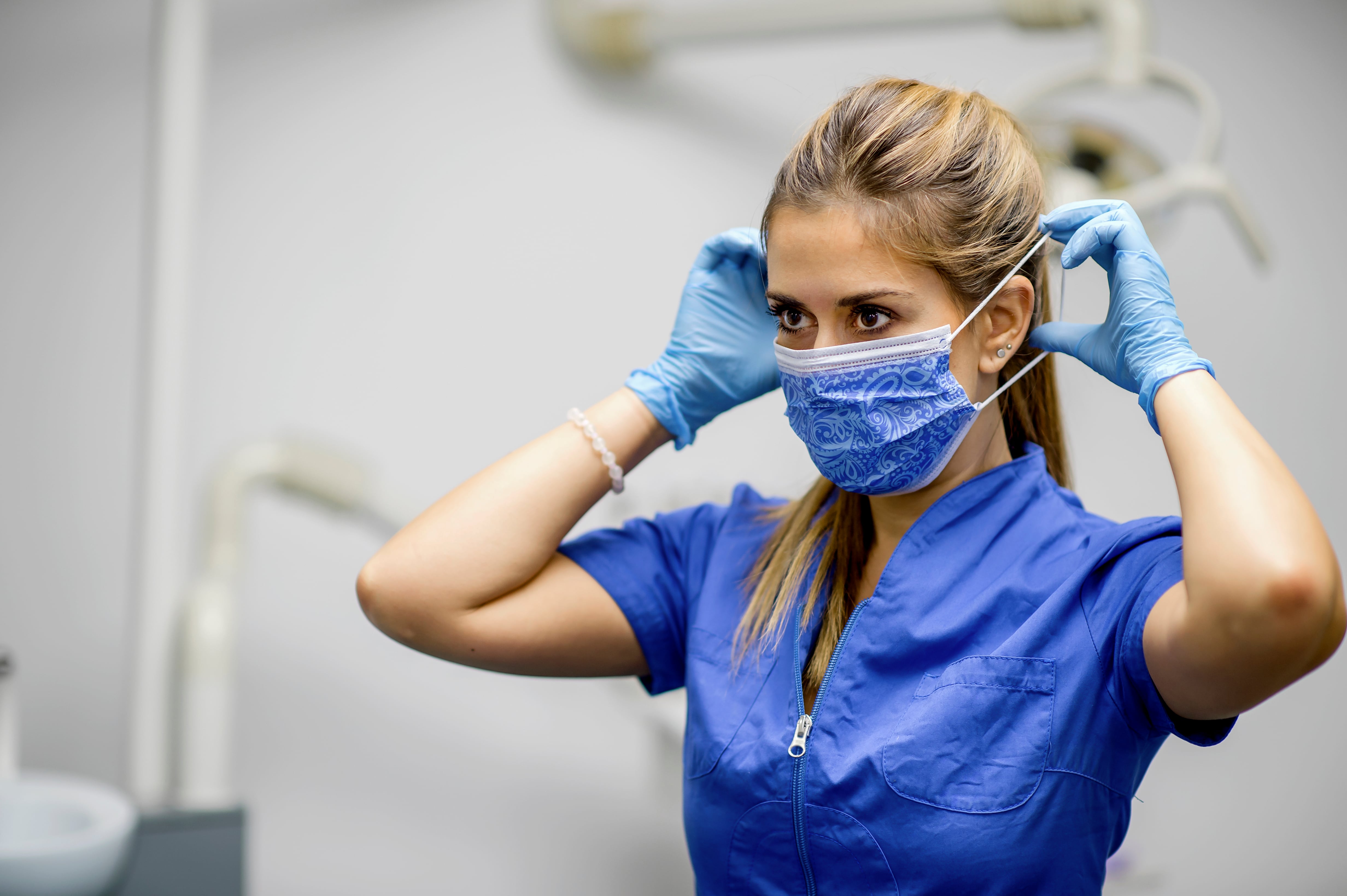 Una sanitaria en su puesto de trabajo poniéndose la mascarilla