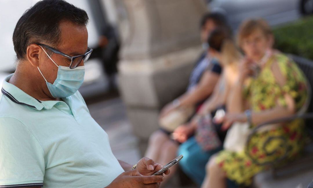 Un ciudadano con mascarilla revisa su teléfono en una calle del centro de Madrid.