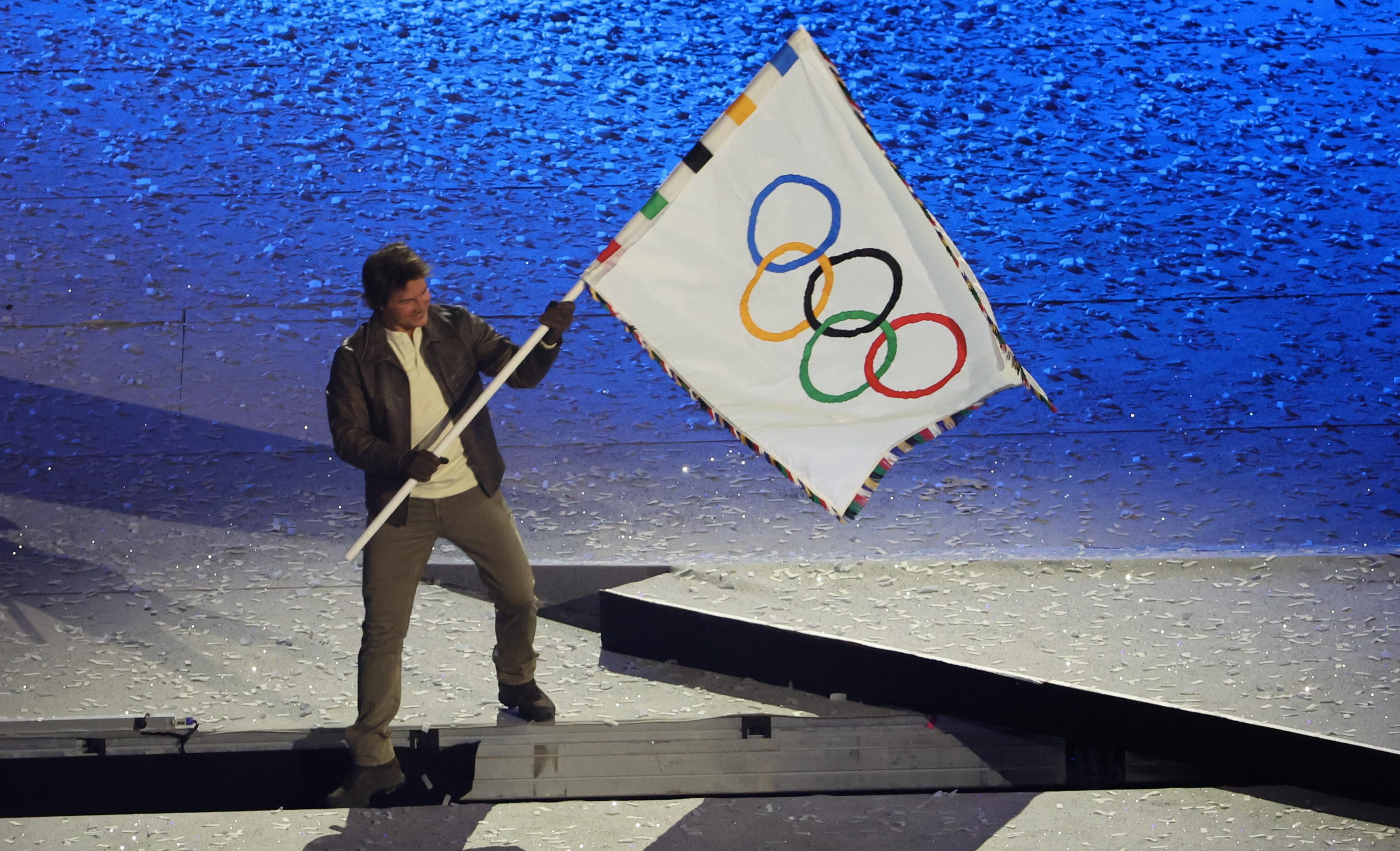 Tom Cruise ondea la bandera de los Juegos Olímpicos en la ceremonia de clausura.