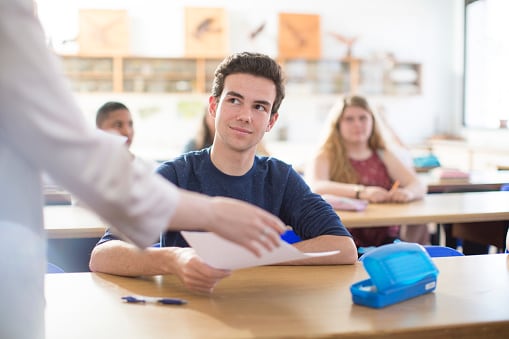 Alumno recibiendo un examen corregido de manos de su profesor