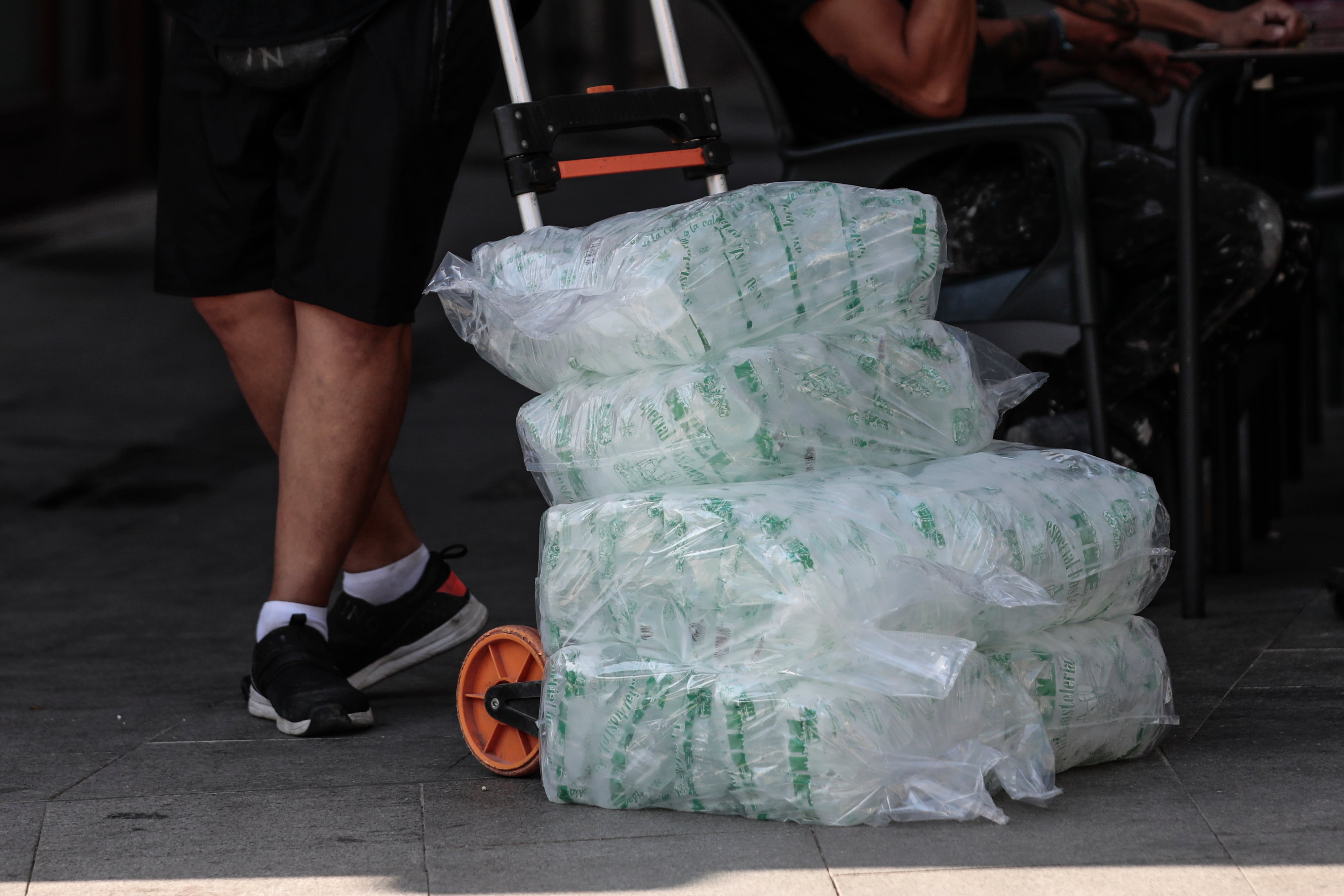 Un repartidor lleva una carretilla cargada con bolsas de hielo