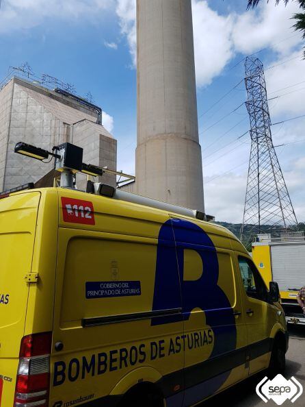 Uno de los vehículos del Bomberos de Asturias frente a la chimenea en la que tuvo lugar el accidente de la central térmica de La Pereda que costó la vida a un trabajador.