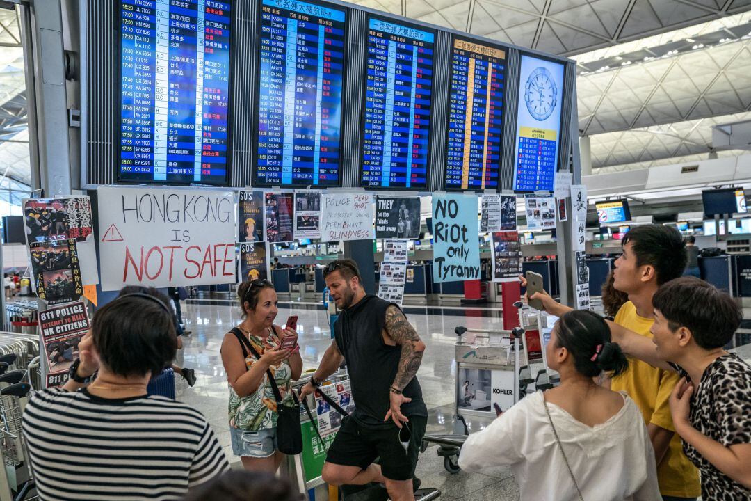 Turistas en los paneles de información del Aeropuerto de Hong Kong en los que se muestran todos los vídeos cancelados 