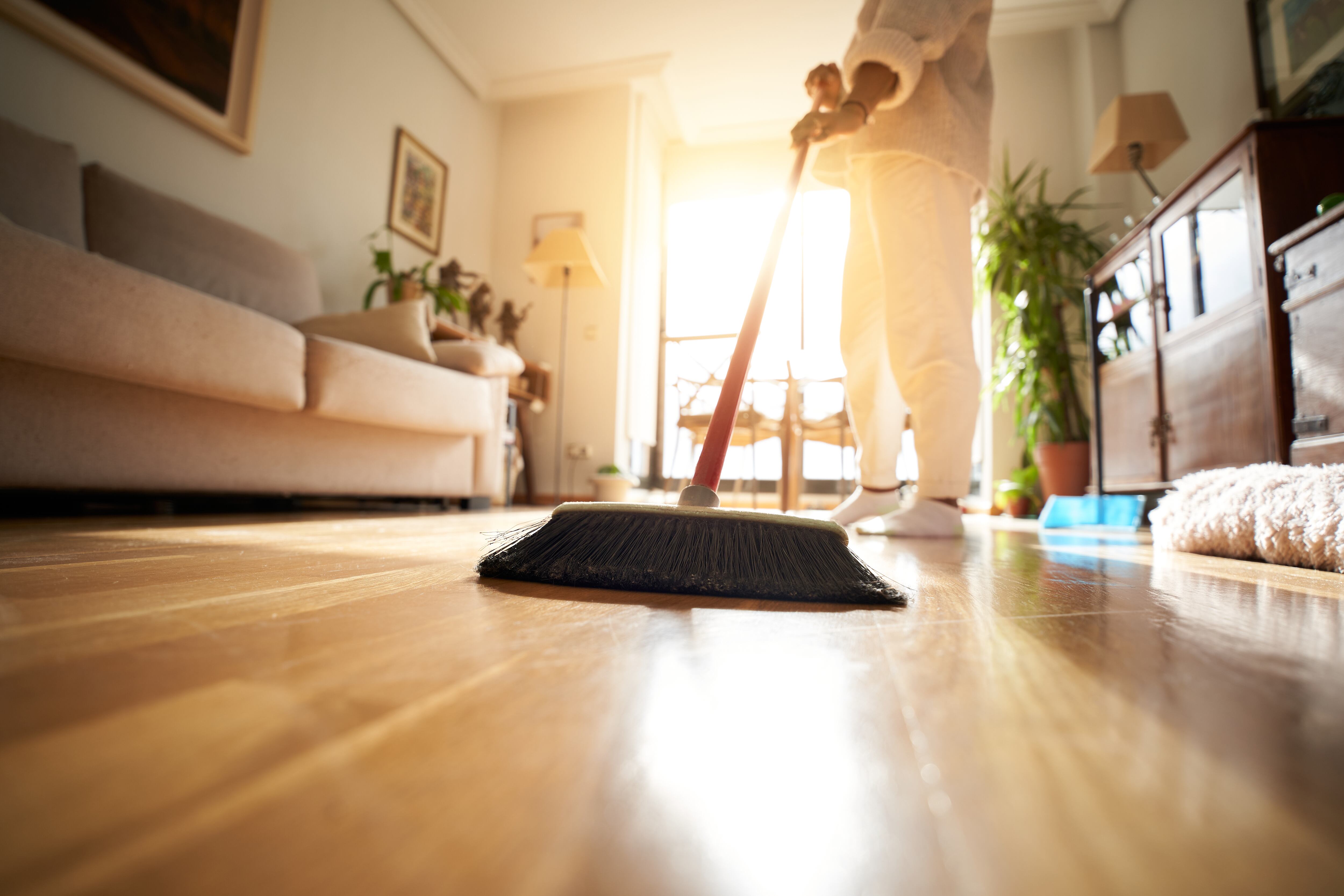 Unrecognizable woman sweeping the parquet floor, window light reflection. Copy space image.