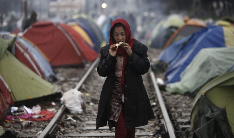 Una mujer come una manzana en una vía de tren junto a tiendas de campaña cerca de Idomeni (Grecia) mientras espera para cruzar la frontera con Macedonia.