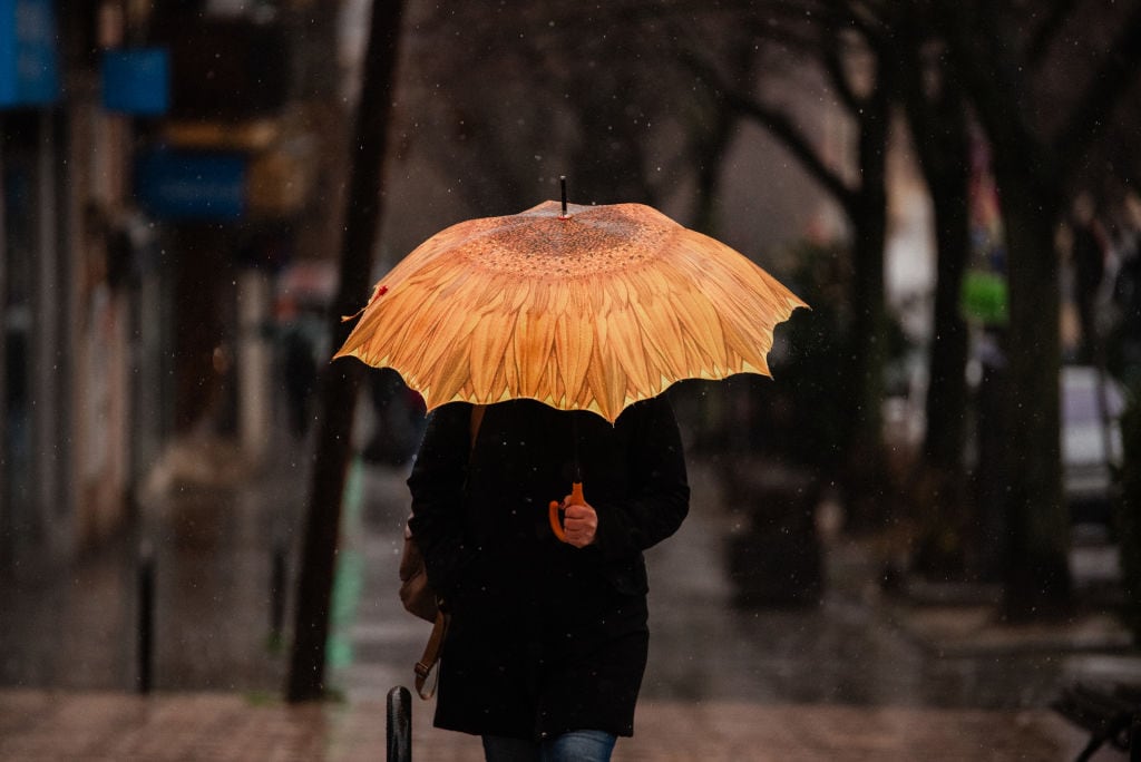 Una persona se protege de la lluvia en Madrid.