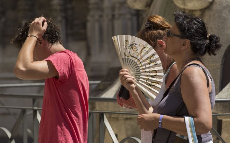 Unos turistas se abanican mientras soportan altas temperaturas haciendo cola para entrar en la Catedral de Sevilla (archivo)