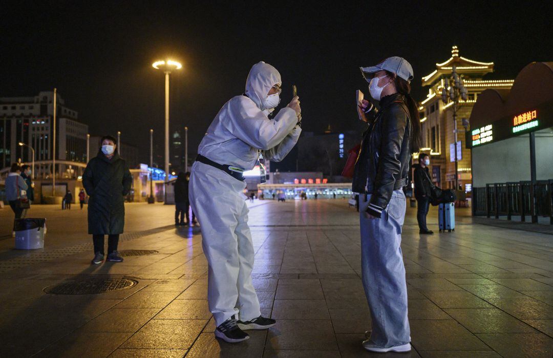 Un hombre con traje protector y marcarilla hace una foto a una mujer que porta mascarilla en la ciudad de Beijing. 