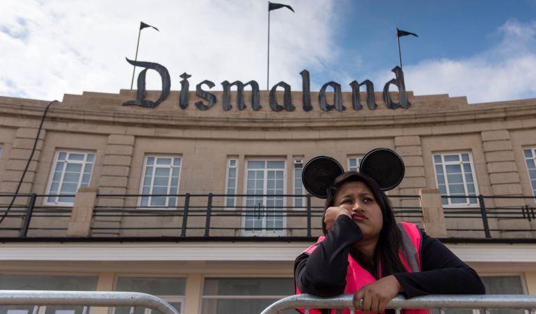 Una persona de seguridad del parque descansa sobre una valla, con gesto aburrido y unas orejas similares a las de Mickey Mouse.