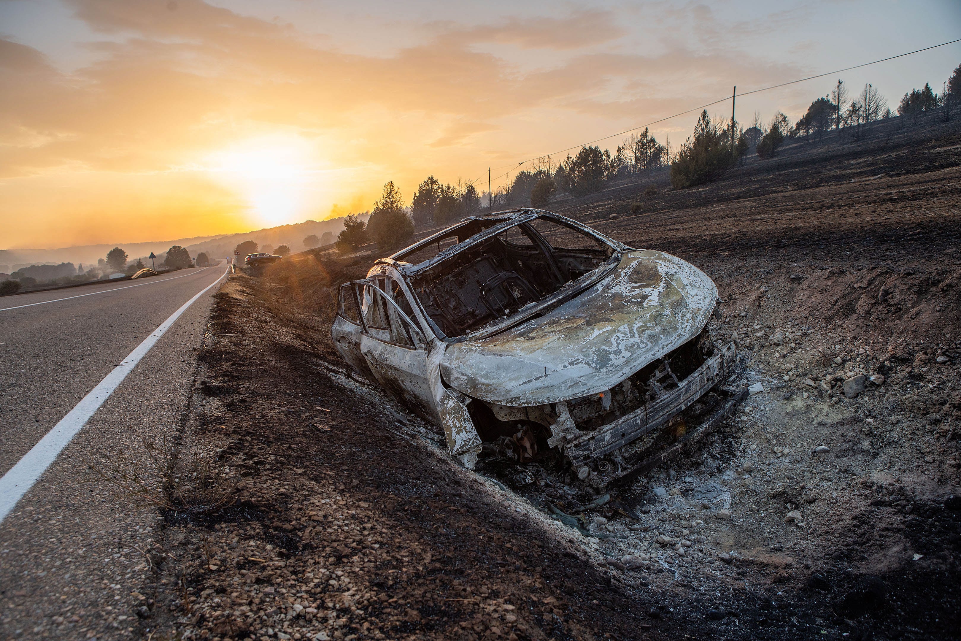 Un coche quemado en la cuneta en el incendio declarado este domingo por la tarde en el término municipal de Quintanilla del Coco, en Burgoa, que ha obligado a evacuar a media docena de municipios, entre ellos Santo Domingo Silos y a los monjes del monasterio románico del mismo nombre.