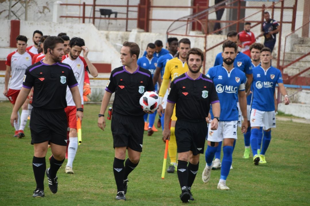 El trío arbitral salta al campo, seguido de futbolistas de Martos y Linares