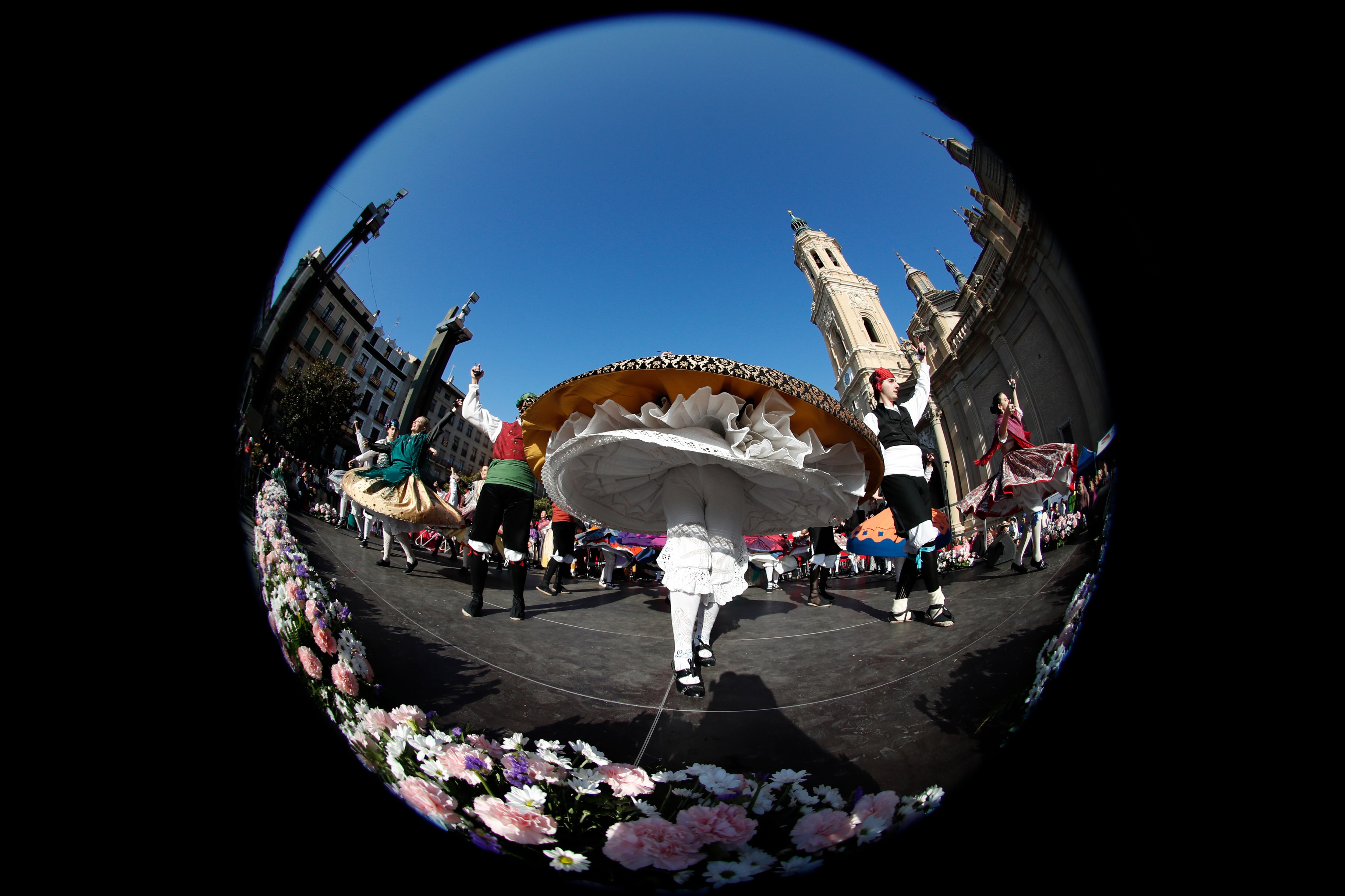 ZARAGOZA, 12/10/2022.- Varias personas bailan junto a la imagen de la Virgen del Pilar que luce ya las primeras flores en una estructura levantada en el centro de la plaza de Zaragoza que lleva su nombre, una ofrenda llena de ilusión que se espera de récord tras dos años de pandemia, con más grupos inscritos que en 2019 y la previsión de alcanzar alrededor de siete millones de flores. EFE/JAVIER BELVER
