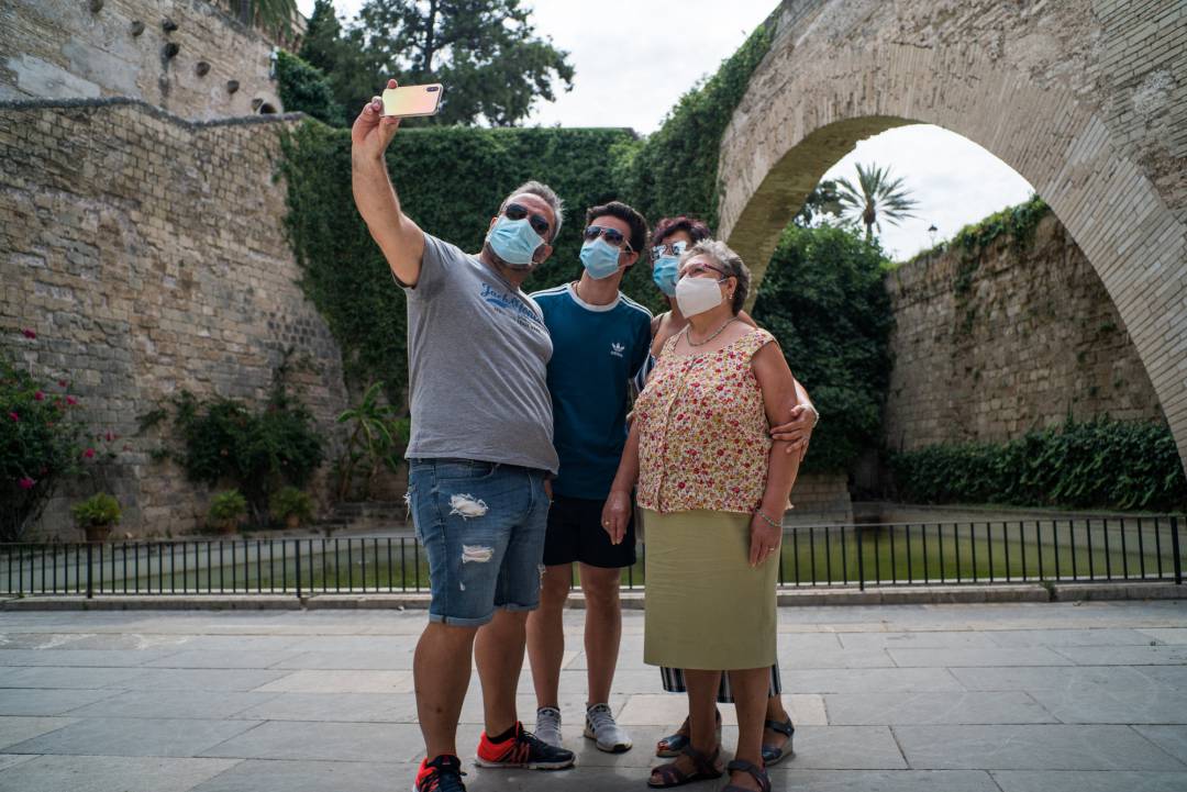 Varios turistas se hacen una foto junto a la Catedral de Santa María de Palma de Mallorca durante el primer día de uso obligatorio de la mascarilla en Baleares por el Covid-19, en Palma de Mallorca, Islas Baleares (España) a 13 de julio de 2020. El uso obligatorio será tanto en espacios cerrados como abiertos aunque se pueda mantener la distancia de seguridad y su incumplimiento podrá acarrear multas de 100 euros. No obstante, habrá algunas excepciones como en las playas y en las piscinas, para la práctica de deporte, consumir bebidas y alimentos o tocar instrumentos de viento.