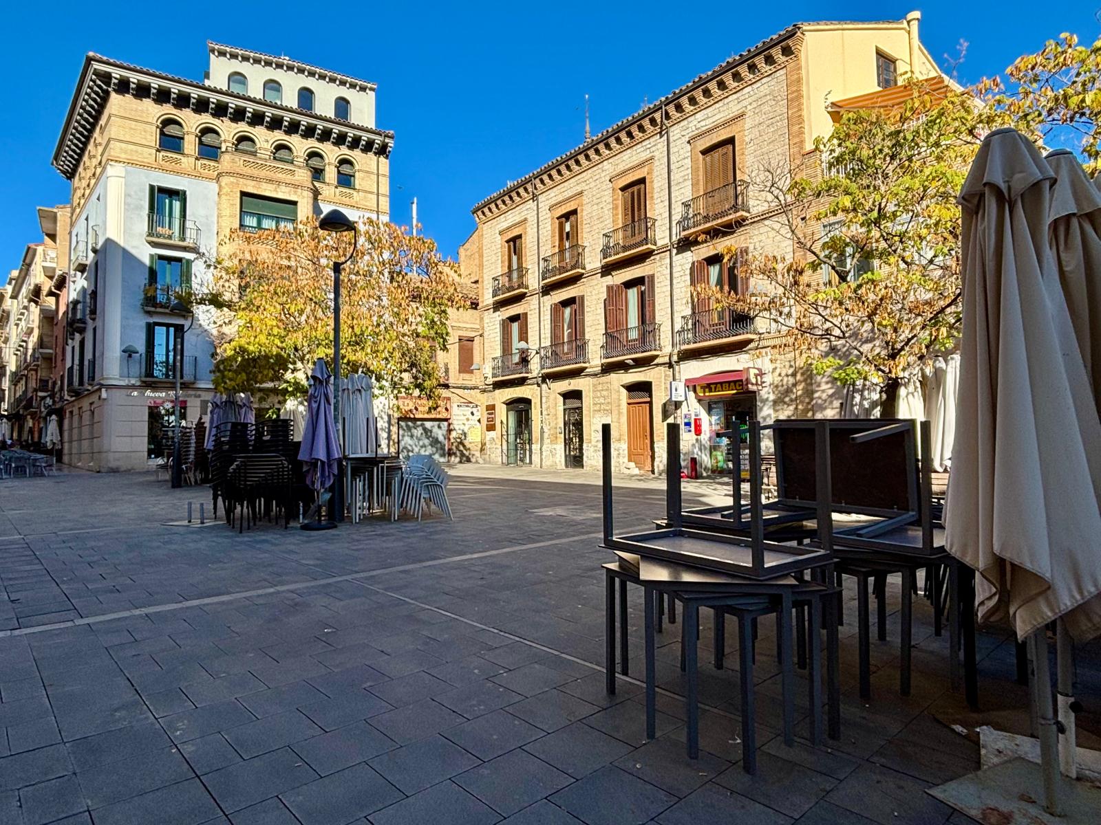 Plaza de Alfonso el Batallador repleta de sillas, mesas y sombrillas apiladas con los bares cerrados