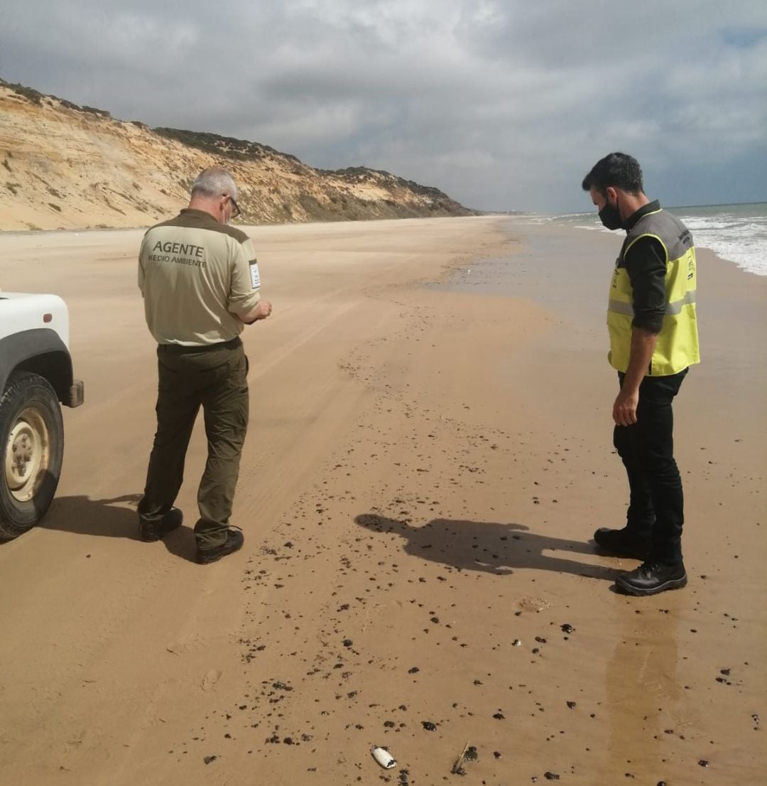 Dos agentes de Medio Ambiente inspeccionan las manchas que han llegado a la playa entre Mazagón y Almonte. 