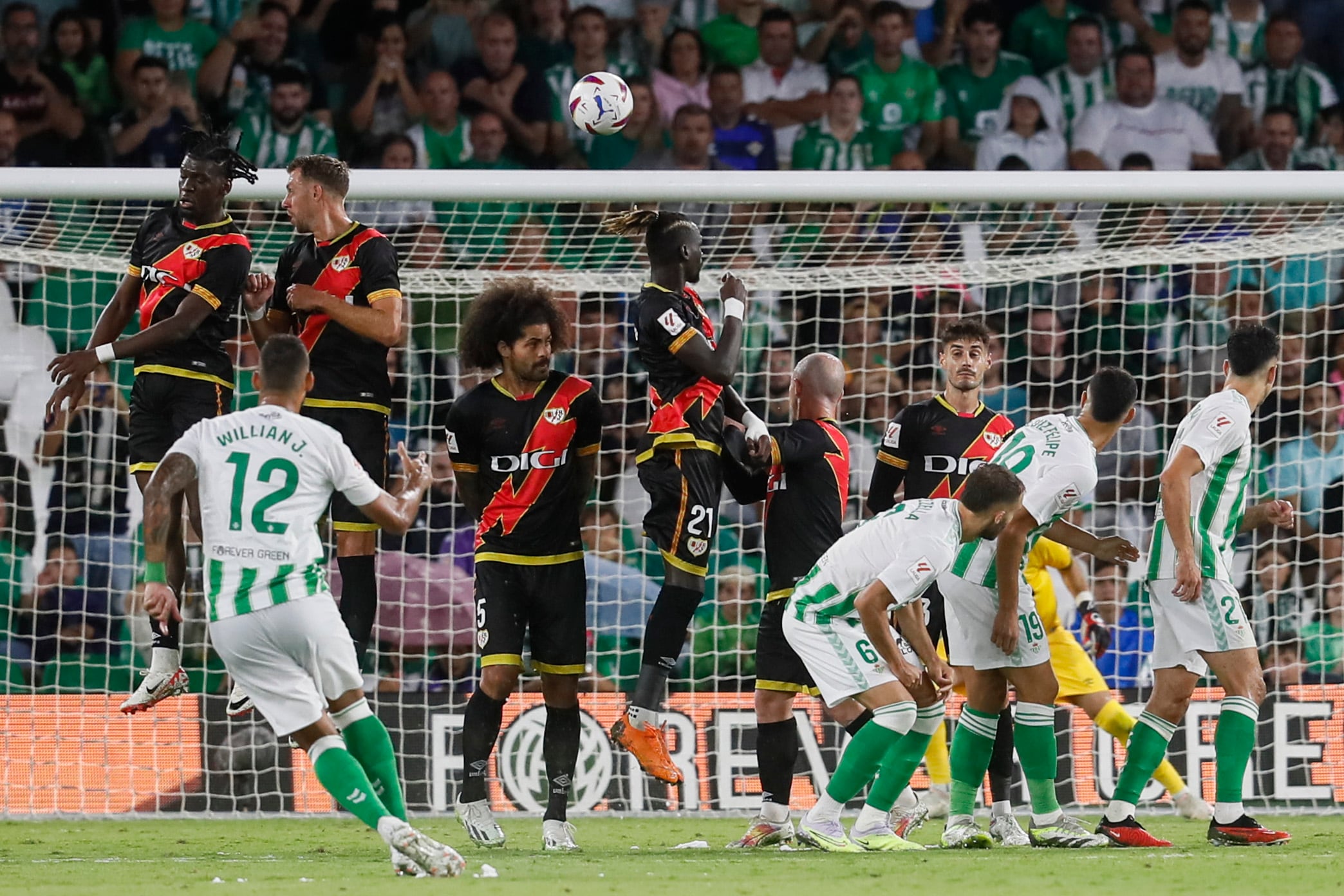 Sevilla, 02/09/2023.- El delantero brasileño del Betis, Willian José (i), tras lanzar la falta directa que ha significado el primer gol del equipo andaluz durante el encuentro correspondiente a la cuarta jornada de primera división que disputan hoy sábado frente al Rayo Vallecano en el estadio Benito Villamarín de Sevilla. EFE/José Manuel Vidal.
