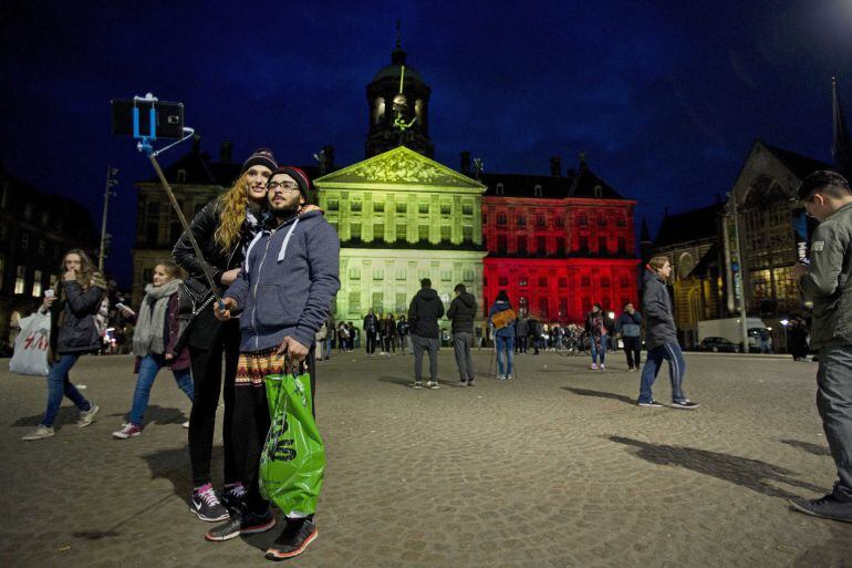 Unas personas posan para las fotos frente al Palacio Real en la plaza Dam de Amsterdam iluminado con los colores de la bandera de Bélgica 