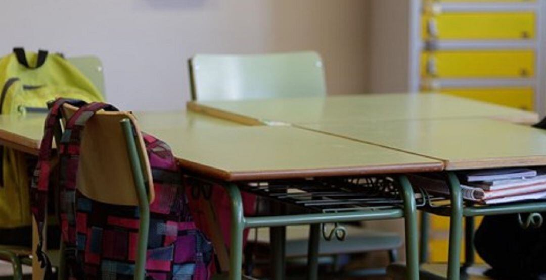 Mesas y sillas con mochilas en un colegio.