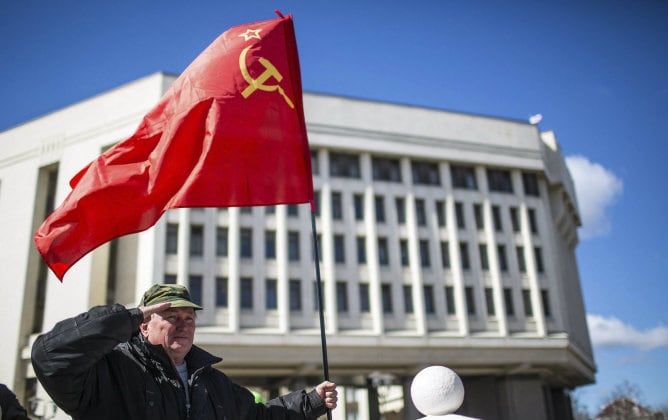 Un hombre sostiene una bandera soviética mientras realiza un saludo militar delante del Parlamento en Simferópol