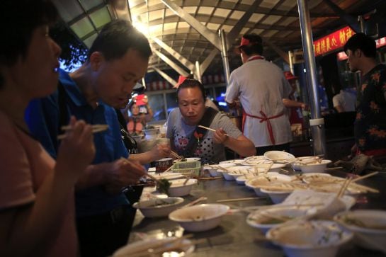 Varios visitantes cenan en un puesto en el mercado nocturno de Donghuamen.