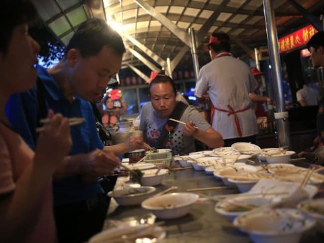 Varios visitantes cenan en un puesto en el mercado nocturno de Donghuamen.