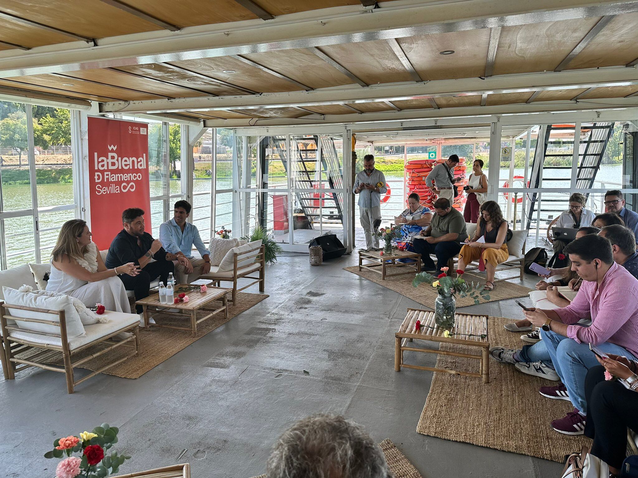 Miguel Poveda, entre la delegada municipal de Cultura, Angie Moreno, y el director de la Bienal, Luis Ybarra, atiende a los medios de comunicación en un catamarán surcando el Guadalquivir