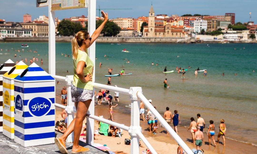 Una turista saluda desde una escalera de la playa de San Lorenzo.