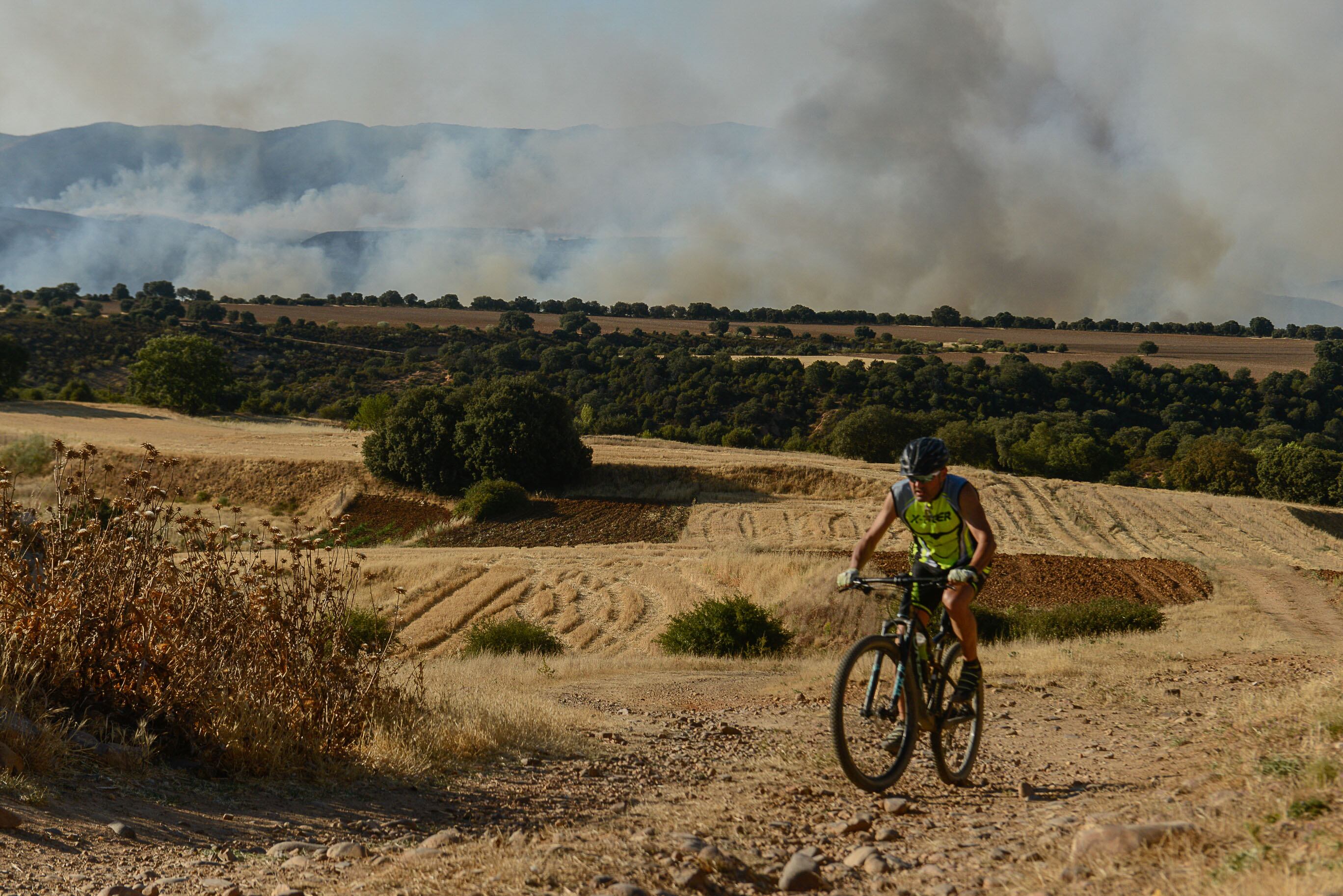 Un ciclista circula cerca del incendio declarado en Valdepeñas de la Sierra (Guadalajara), el pasado martes