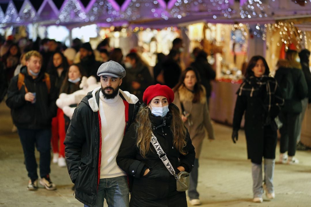 Una pareja con mascarilla pasea por un mercado navideño.