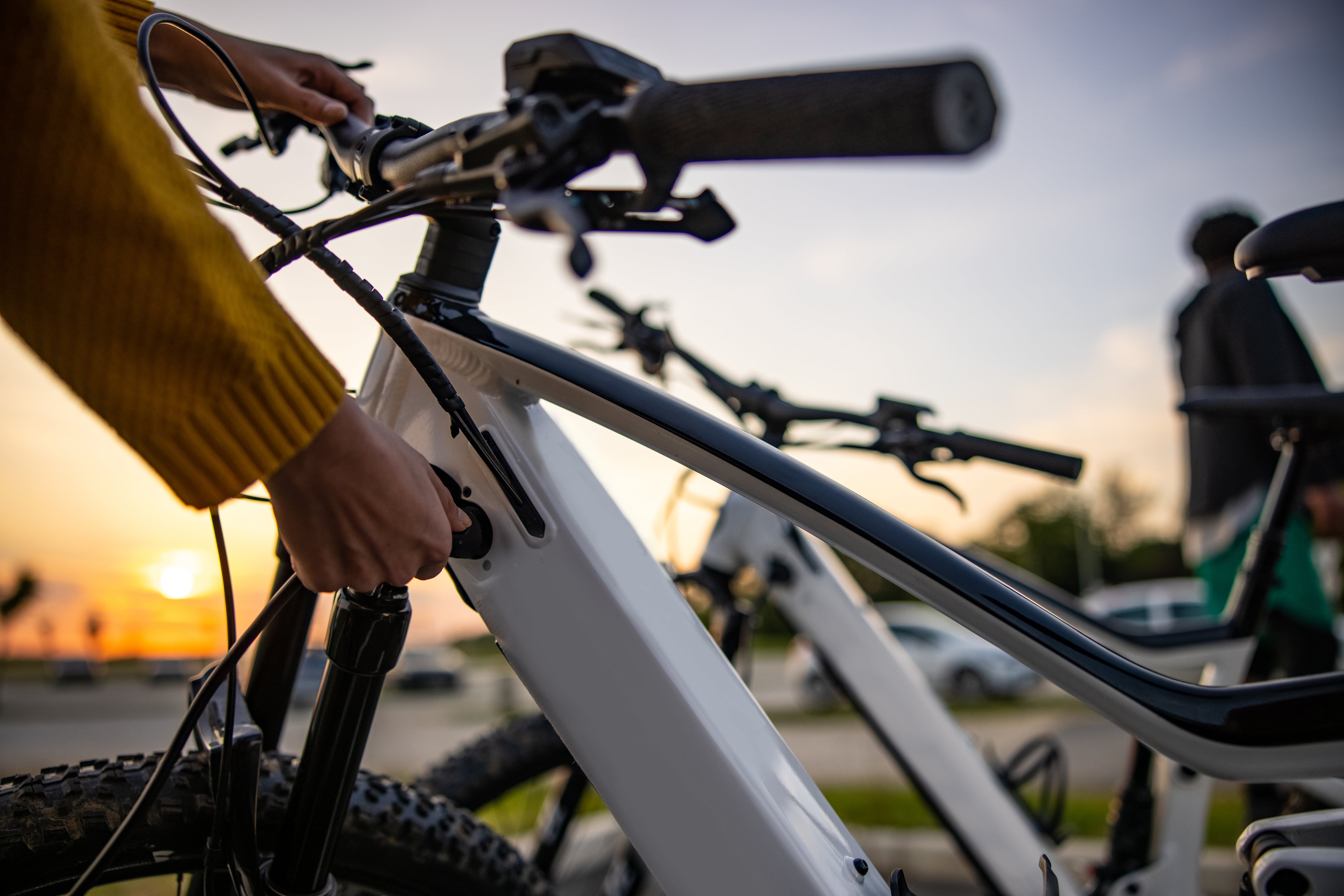 Close up of woman&#039;s hand inserting plug into electric bicycle for charging at electric charging station