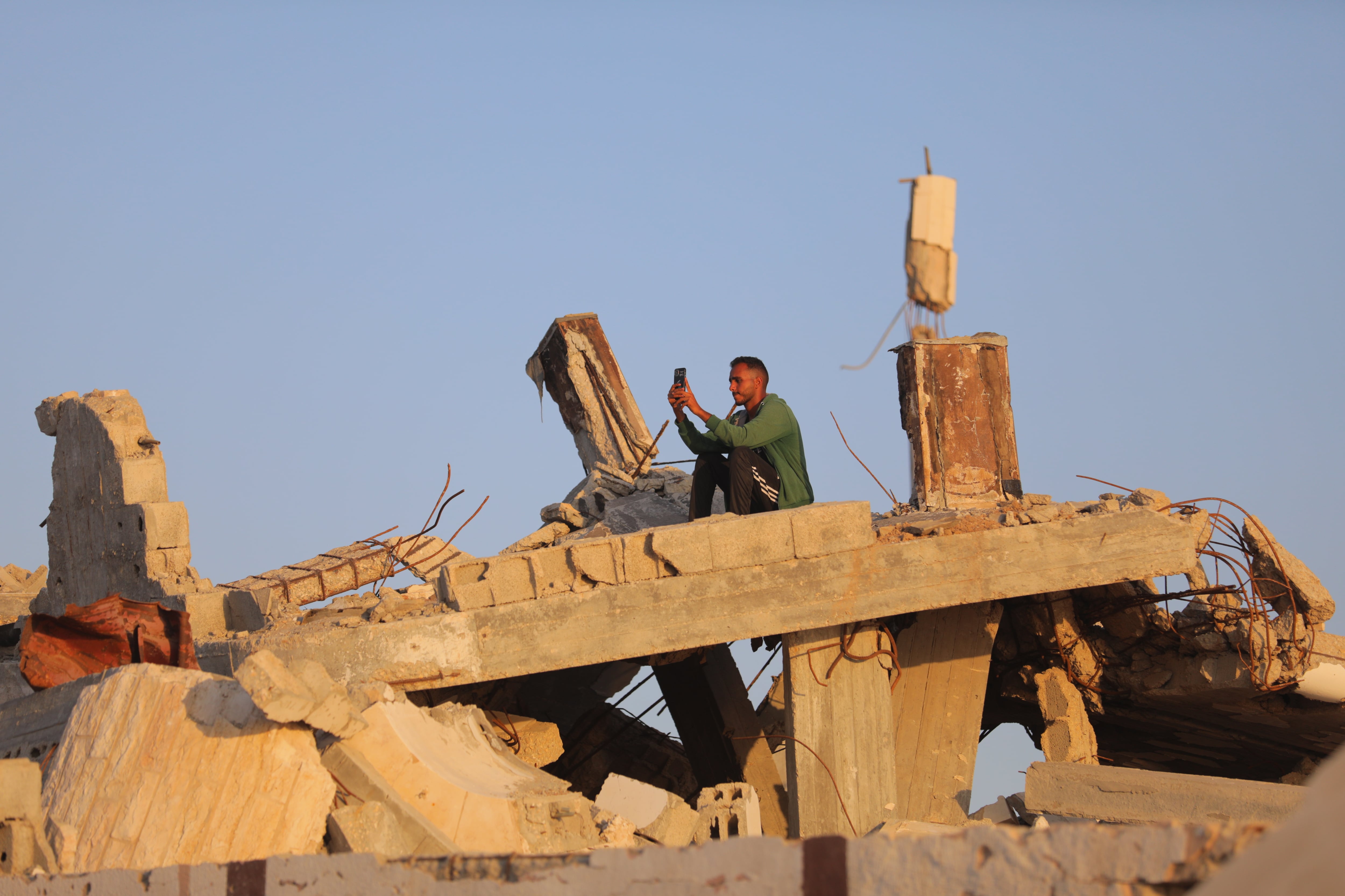 Un gazatí intentando encontrar conexión para su móvil entre los escombros en Nuseirat