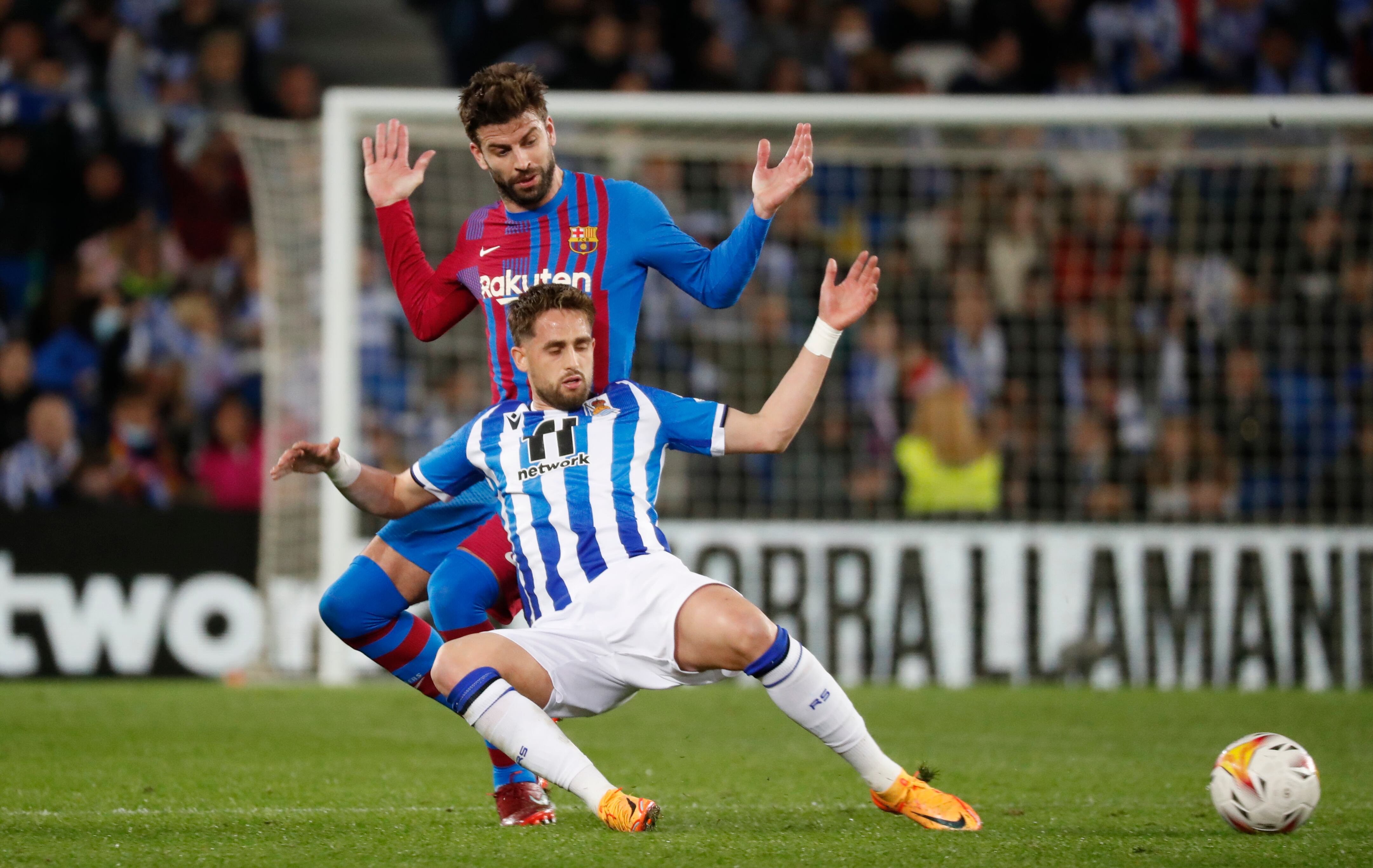 SAN SEBASTIÁN, 21/04/2022.- El centrocampista belga de la Real Sociedad, Adnan Januzaj, cae ante el defensa del FC Barcelona, Gerard Piqué, durante el encuentro correspondiente a la jornada 33 disputado hoy jueves en el Reale Arena de San Sebastián. EFE / Juan Herrero.
