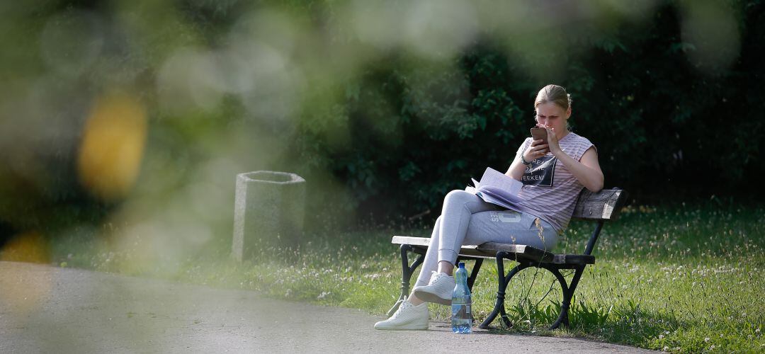 Una joven consulta el móvil en una pausa en su lectura de un libro en un parque.