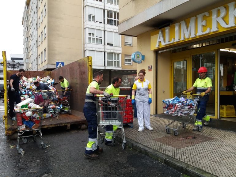 Personal de Alimerka y operarios sacan la mercancía del supermercado incendiado y lo tiran directamente a un contenedor de basura.