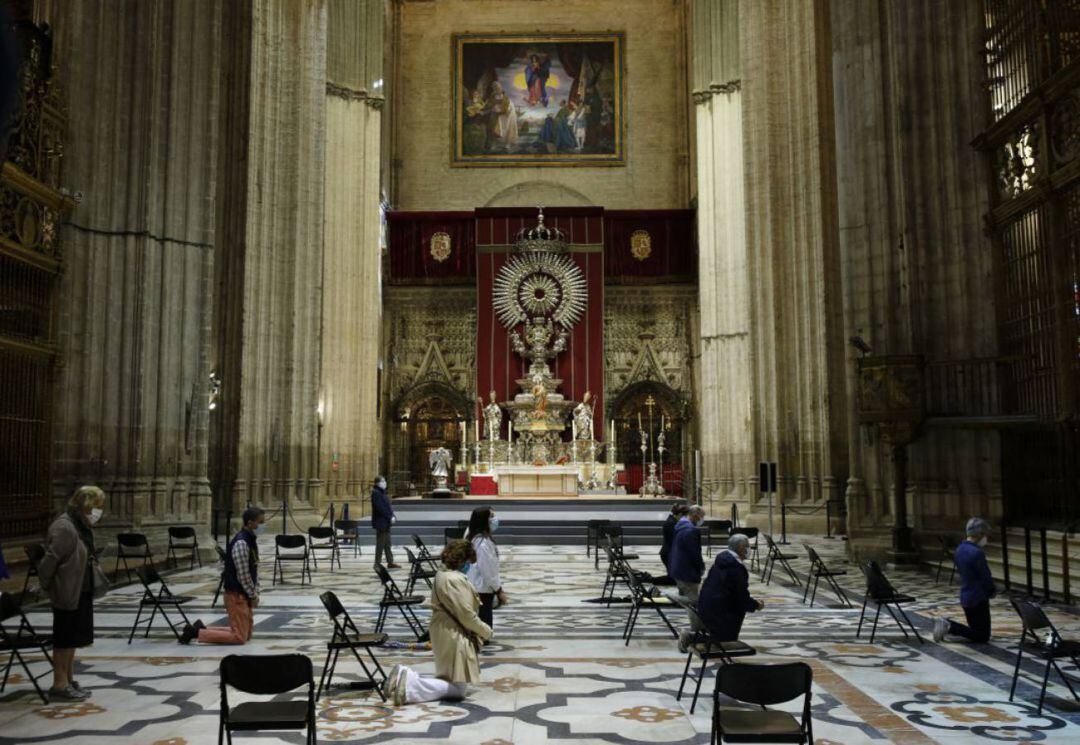 Misa ante el altar mayor de la Catedral de Sevilla, con fieles que mantienen las distancias de seguridad y mascarillas