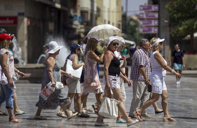 GRA335. VALENCIA, 6/07/2015. Un grupo de turistas se protegen del intenso sol con sombreros o paraguas mientras caminan por la plaza de la Virgen. Valencia continúa afecta por la ola de calor y se encuentra en alaerta naranja por temperaturas de hasta 40
