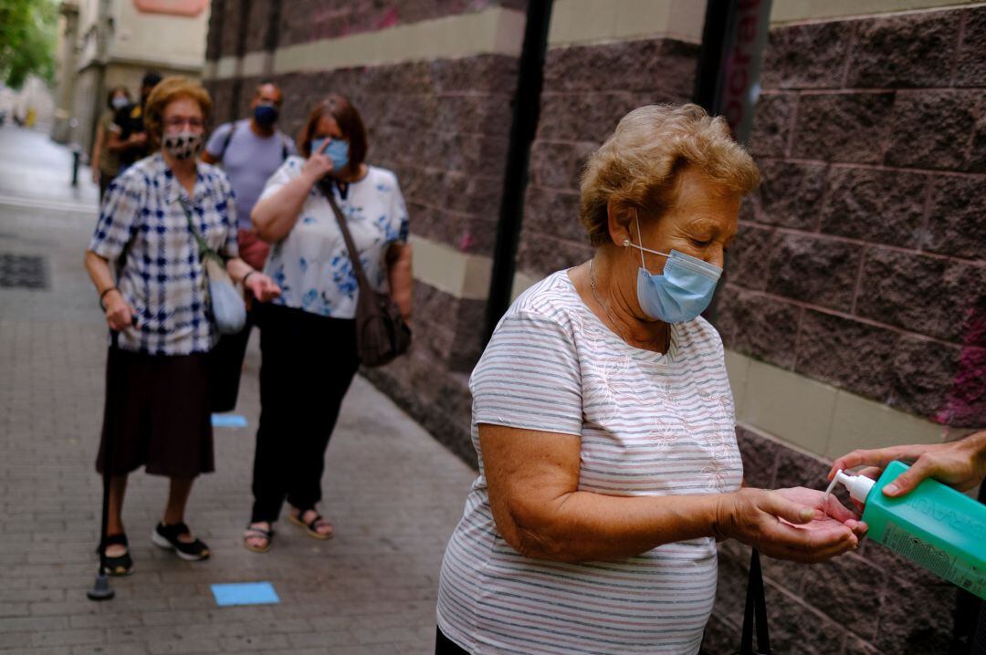 Un voluntario dispensa gel hidroalcohólico en las manos de una mujer antes de someterse a una prueba PCR, en una imagen de archivo