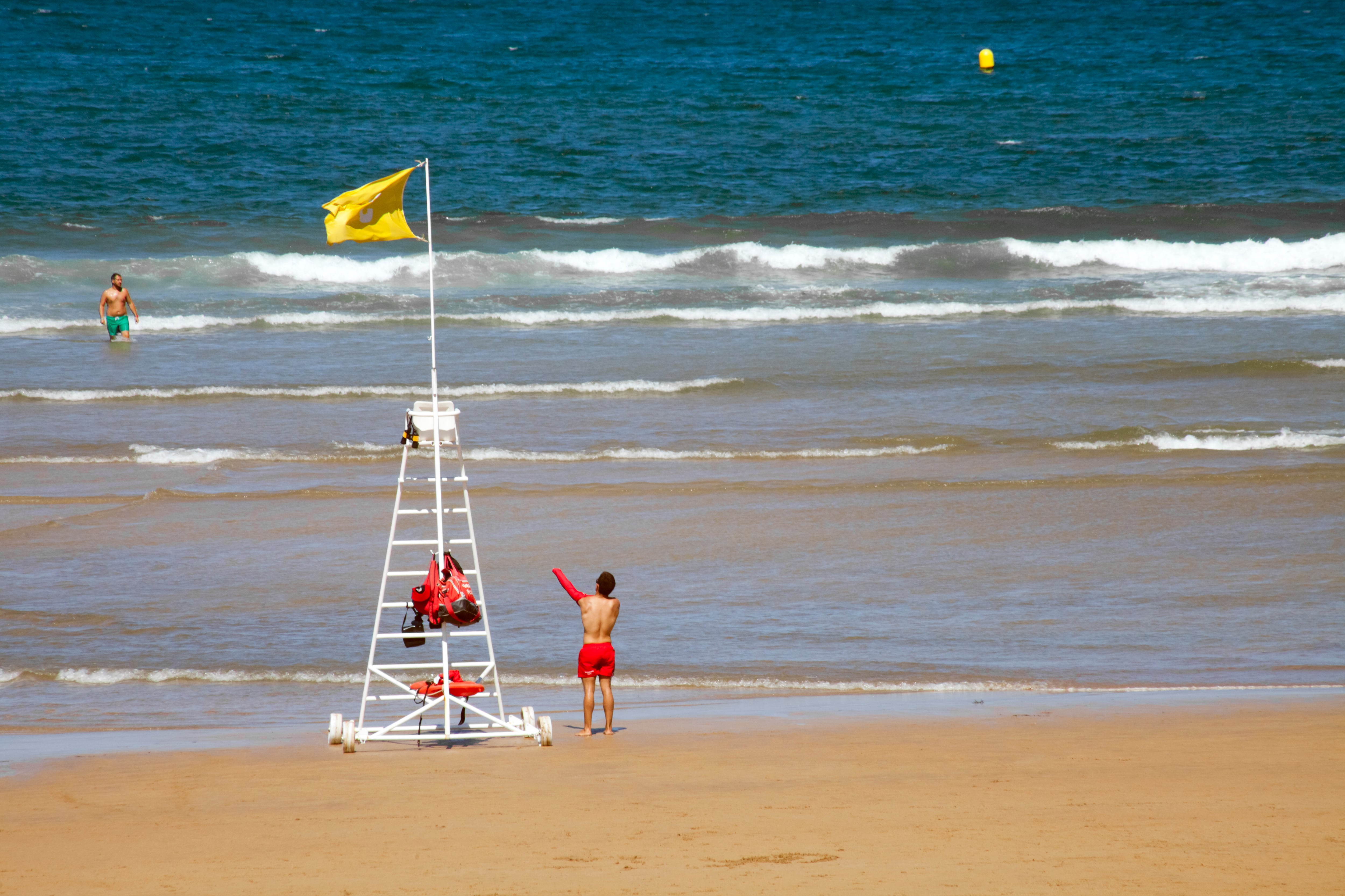 Gijon, Spain-August 31, 2018:Life guard in San Lorenzo beach in Gijón, Asturias, Spain. Incidental people in the beach,  sunny summer weather, yellow flag on lifeguard chair. Copy space on the right.