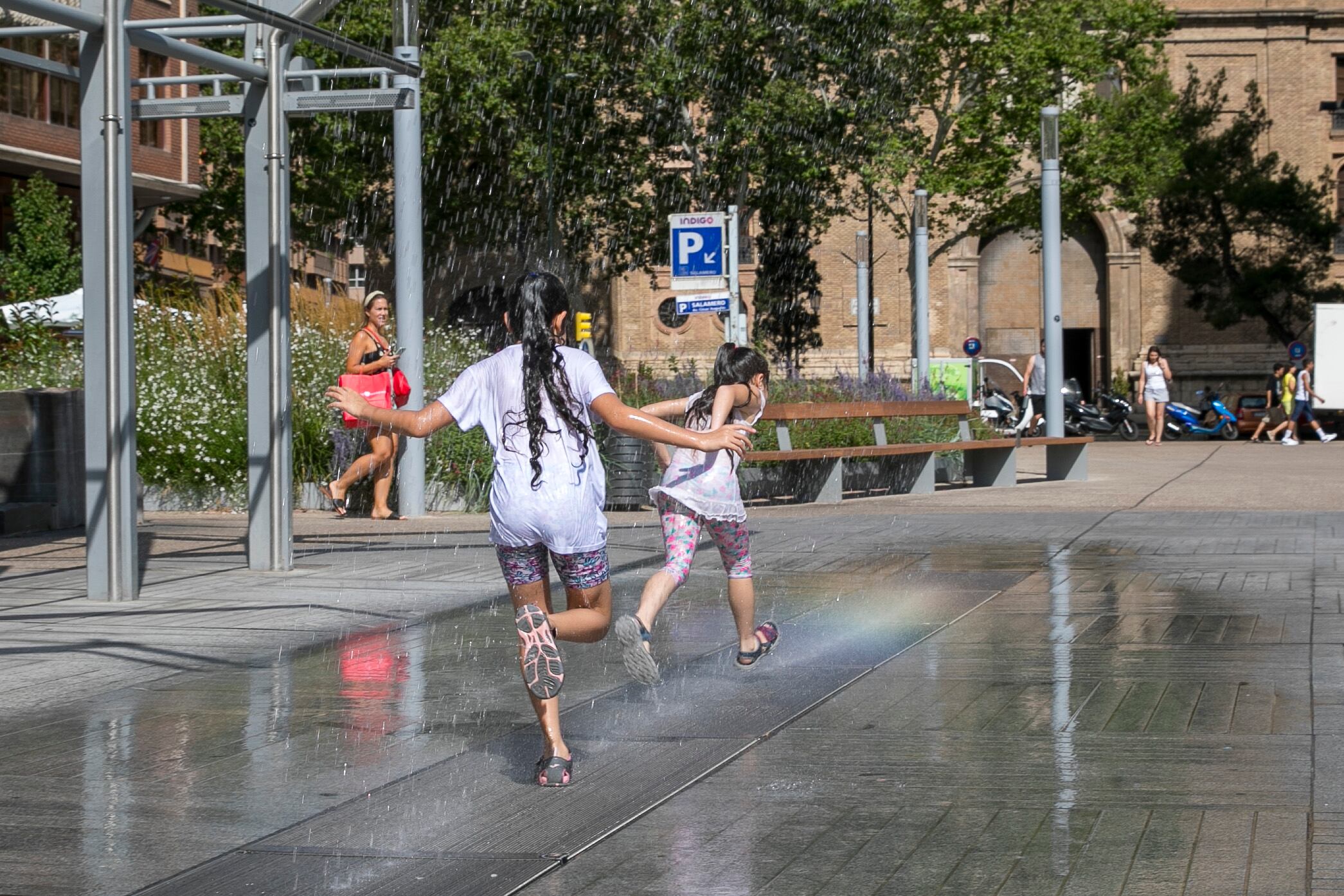 Unas niñas se refrescan en unos chorros de agua en Zaragoza. EFE/Javier Cebollada