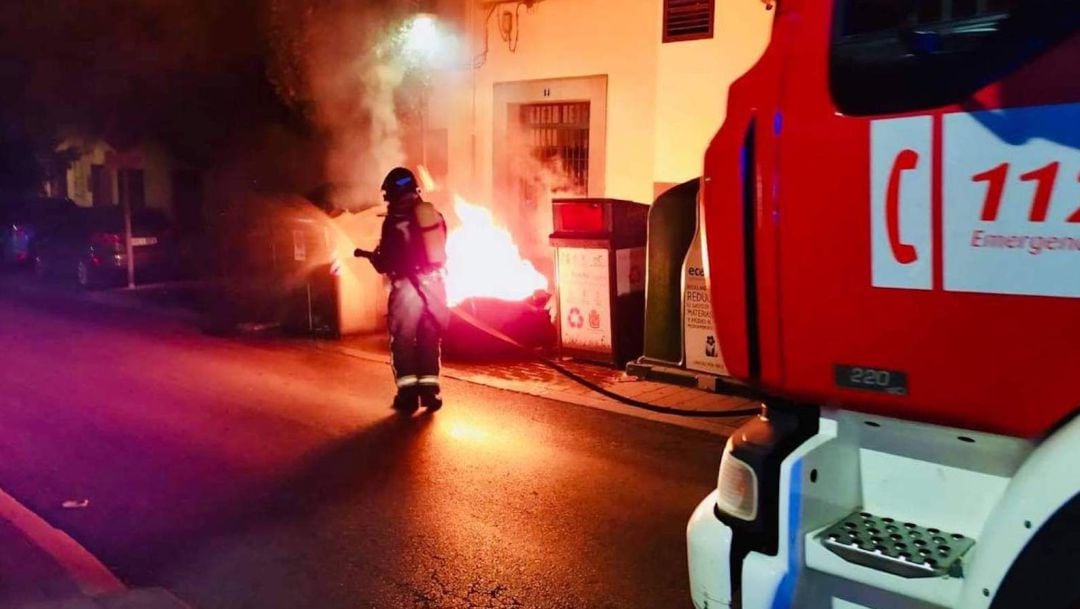 Un bombero apaga uno de los contenedores incendiados.