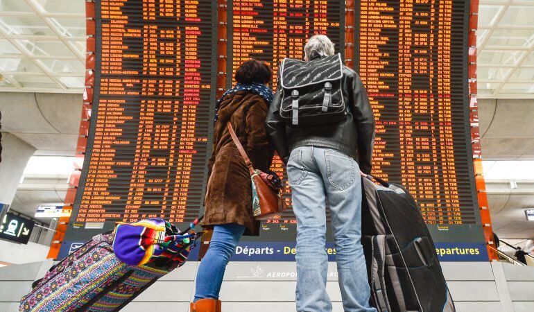 Dos personas buscan su vuelo en el panel de un aeropuerto.