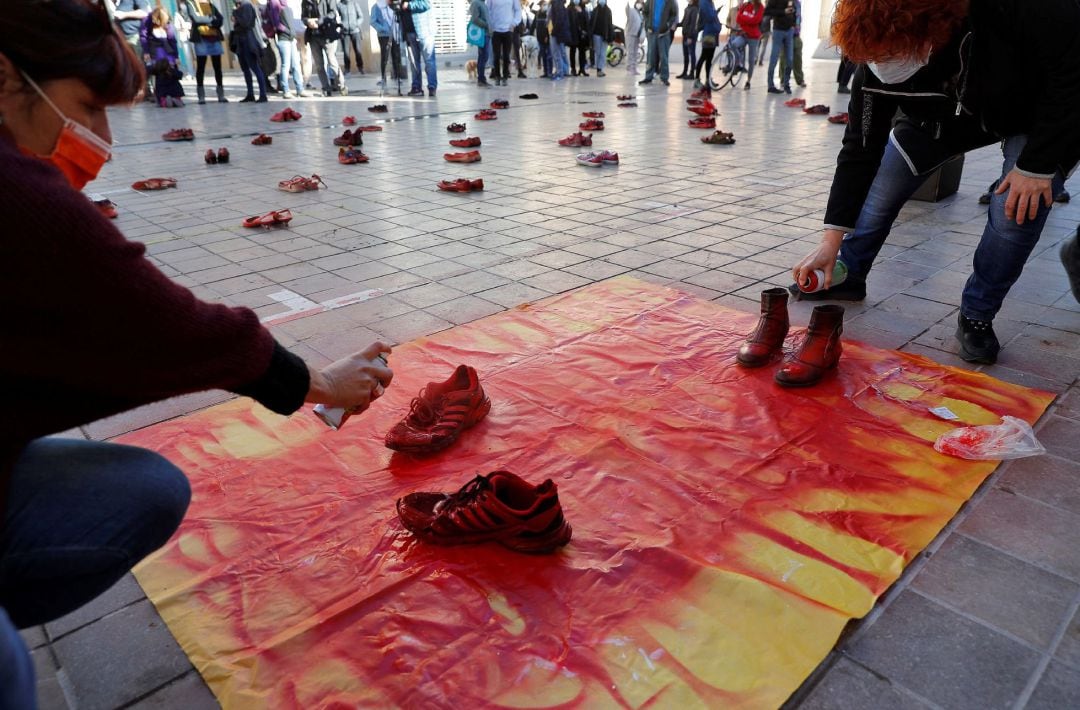 Dos mujeres pintan de rojo dos pares de zapatos en la plaza de Benimaclet de Valencia en una de las acciones y mobilizaciones organizada por la Assemblea Feminista de València con motivo del Día Internacional para la Eliminación de la Violencia contra las Mujeres.