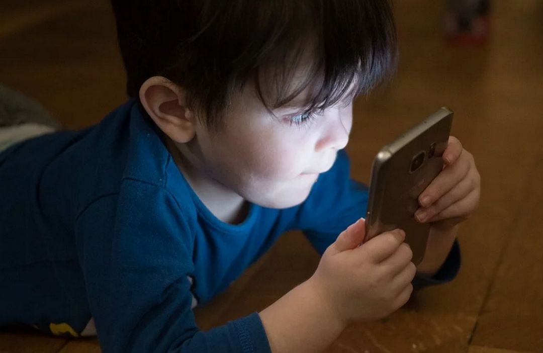 Un niño frente a una pantalla de móvil. 