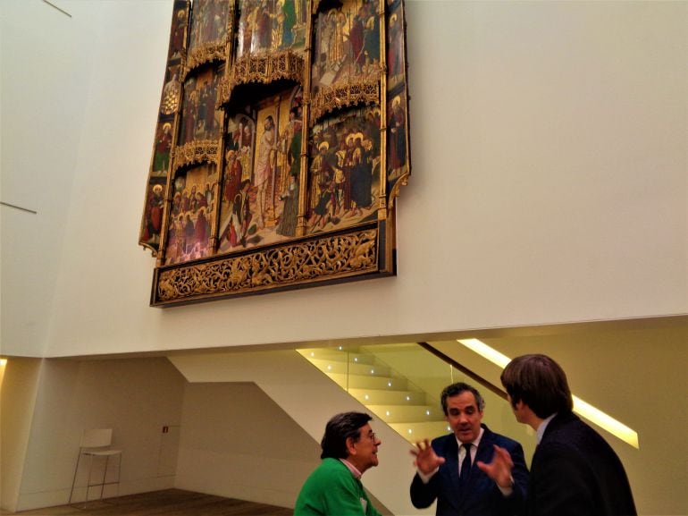 Bajo el espectacular retablo del siglo XV, el director del Museo, Alfonso Palacio, conversa con el concejal de Cultura de Oviedo, Roberto Sánchez Ramos, y el director general de Cultura, Vicente Domínguez